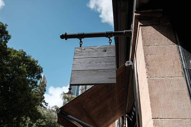 Old blank black wooden sign hanging on a building wall with sky above.