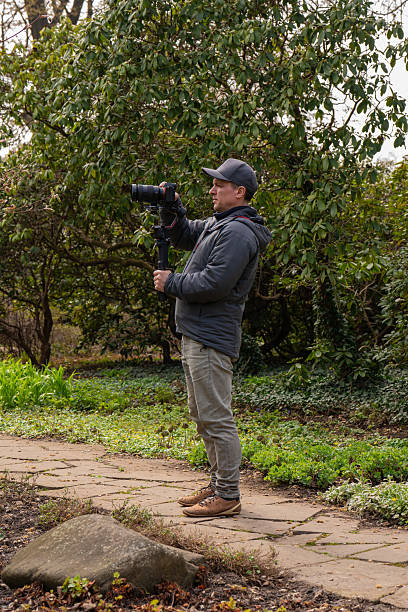istock Man with professional camera on stabilizer records video blossoming trees in city park. Creative process nature photography. Suitable for photography, videography, technology, content creation. 2207449107