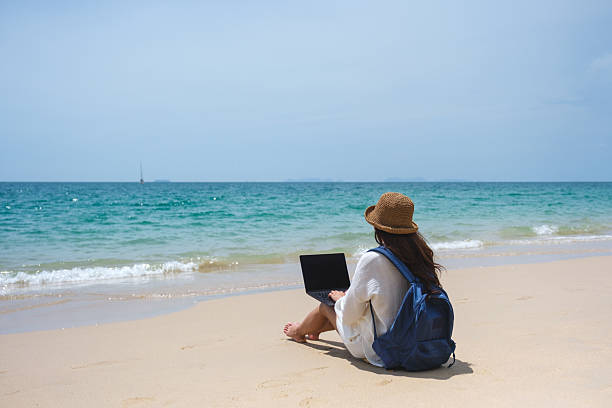 istock A female traveler using and working on laptop computer while sitting on the beach 2207456551