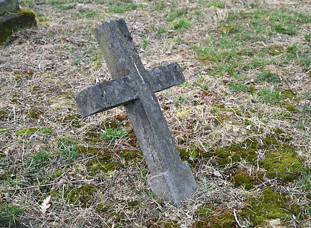 istock Old, weathered cross in a graveyard surrounded by overgrown grass and moss 2207457358