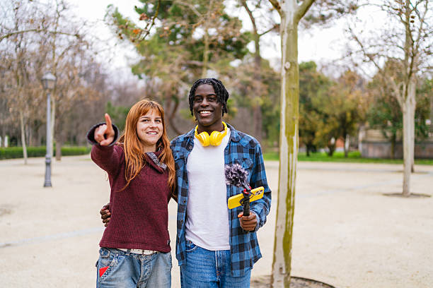 istock Young multiracial couple vlogging in a park, filming and pointing 2207459377