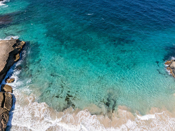 Pristine sandy beach with turquoise waves gently crashing ashore. Rugged rock formations jut into the sea. Picturesque seaside landscape ideal for travel and nature enthusiasts.