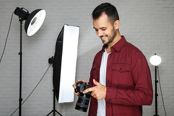 istock Young photographer with camera and professional studio equipment on grey background 2207468833