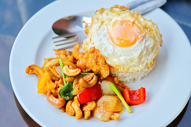 Stir-fried chicken with cashew nuts, white rice and fried egg on a black glass table. Close-up Thai food meal with natural light.