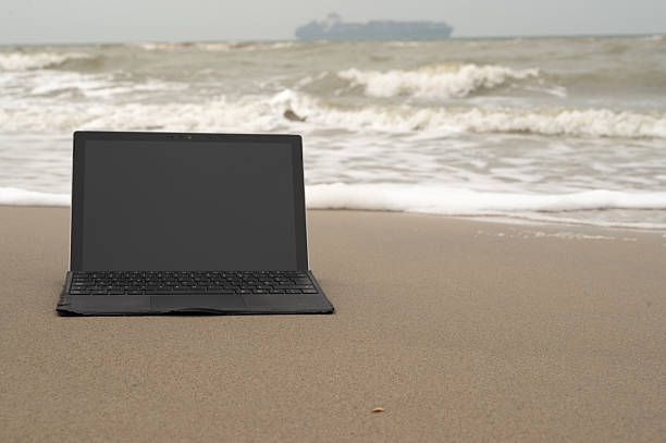 Explore the unique blend of modern technology and serene tranquility by using a laptop on a sandy beach