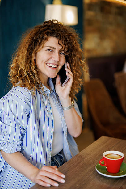 istock Curly woman talking on the phone at the restaurant while drinking coffee 2207483111