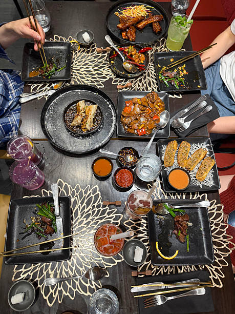 istock Image of top-down view of shared asian feast with blue pea juice, dumplings, spring rolls, dipping sauce in cozy chinese restaurant setting 2207484422