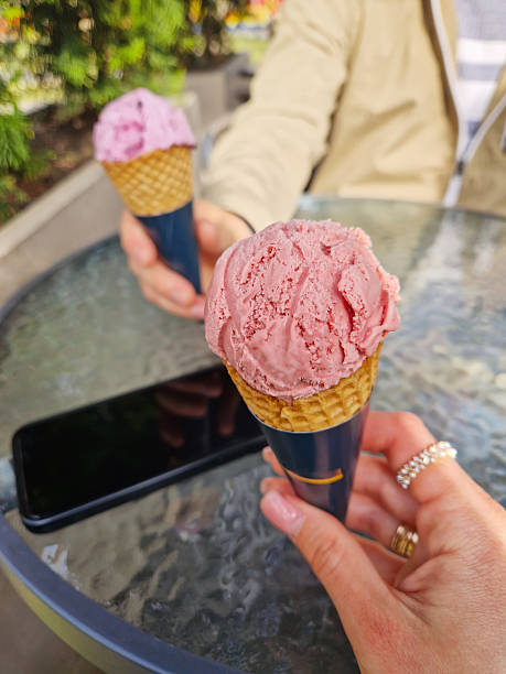 Couple hands holding two ice-cream cones at a table outdoors enjoying a sunny day