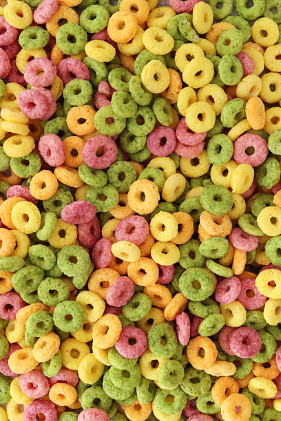Full frame image of surface level of fruit flavoured, multi coloured breakfast cereal, crunchy O-shapes of cereal flours (wheat, oat, maize), sugar, yellow, red, green and orange, elevated view