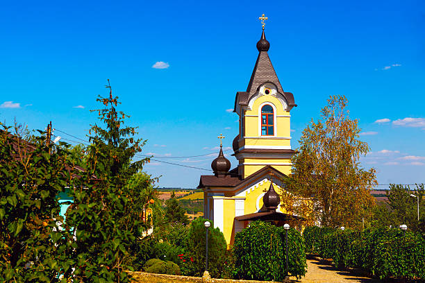 View of monastery in village Tipova from Moldova.  serene church stands tall against a vibrant blue sky, its pale yellow facade a beacon in the countryside