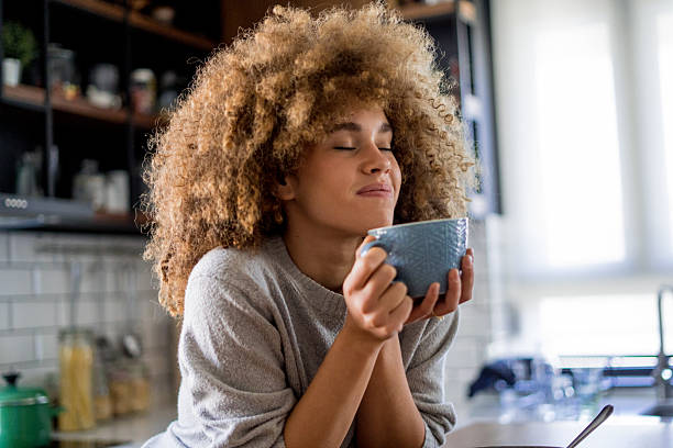istock A young, beautiful woman with natural curls enjoys drinking coffee in a bright, modern kitchen. 2207490874