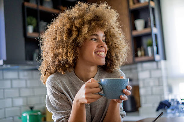 istock A young, beautiful woman with natural curls enjoys drinking coffee in a bright, modern kitchen. 2207490890