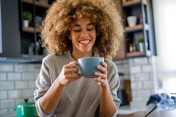 istock A young, beautiful woman with natural curls enjoys drinking coffee in a bright, modern kitchen. 2207490916