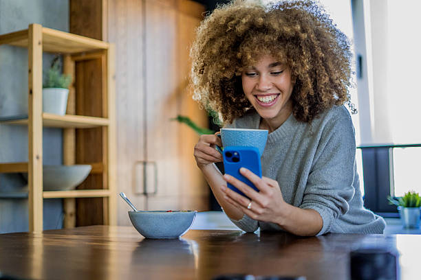istock A young woman with natural curls is enjoying a cup of coffee while casually browsing her smartphone in a bright, modern kitchen 2207491037