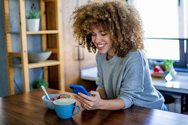 istock A young, beautiful woman with a smile eats a healthy breakfast, enjoying muesli while happily using smartphone 2207491135