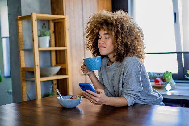 istock A young woman with natural curls is enjoying a cup of coffee while casually browsing her smartphone in a bright, modern kitchen 2207491139