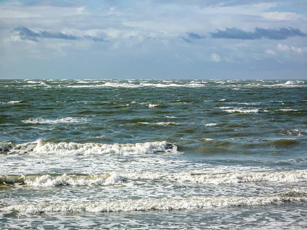 The ocean is calm and the sky is cloudy. The water is a deep blue color. The sky is overcast and the waves are small