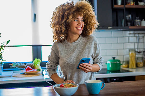istock A young woman with natural curls is enjoying a cup of coffee while casually browsing her smartphone in a bright, modern kitchen 2207491439