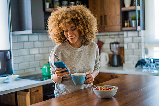 istock A young woman with natural curls is enjoying a cup of coffee while casually browsing her smartphone in a bright, modern kitchen 2207491440