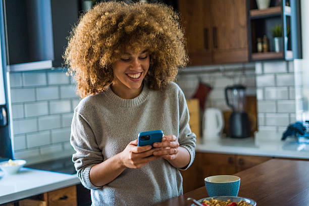 istock A young woman with natural curls is enjoying a cup of coffee while casually browsing her smartphone in a bright, modern kitchen 2207491441