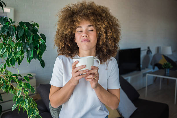 istock A young, beautiful woman with natural curls sits on a comfortable sofa by the window, surrounded by greenery, enjoying her coffee. A morning ritual, the comfort of home 2207492263