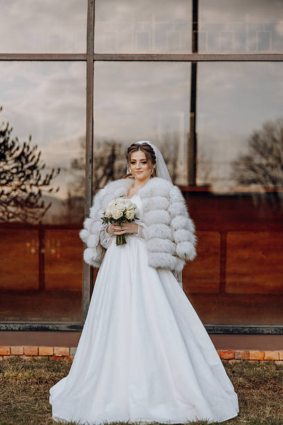 istock A bride is standing in front of a window, wearing a fur coat 2207492464