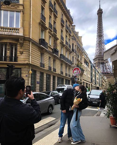 Paris, France: Man Photographs Affectionate Tourists Near Eiffel Tower Paris, France: A man photographs an affectionate couple on Avenue Rapp in the 7th arrondissement, with the Eiffel Tower in the background. three way kiss stock pictures, royalty-free photos & images