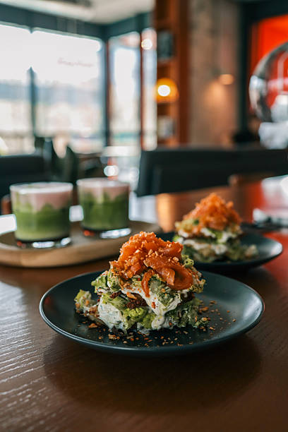Close-up of a gourmet salad stack with creamy dressing and caramelized onions, served on a dark plate in a cozy modern cafÃ© setting with blurred background