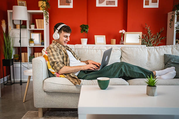 istock cheerful young man with headphones lying down on sofa and use laptop 2207524957