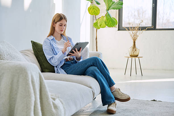 istock Young woman using digital tablet sitting on sofa at home 2207527678