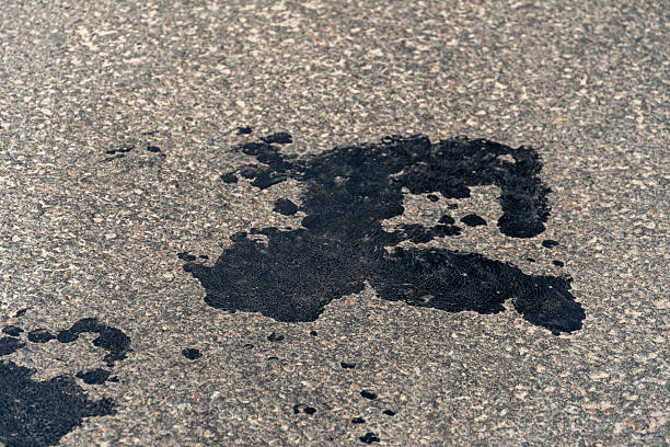 A dark, viscous stain on a concrete surface indicates a possible oil or chemical leak in an urban environment. This marks the aftermath of recent rain