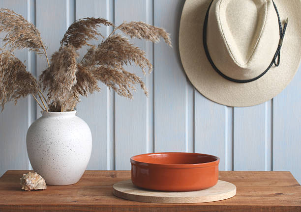 Modern interior design with empty terracotta bowl, pampas grass, hat and seashell on wooden table with light blue wooden wall