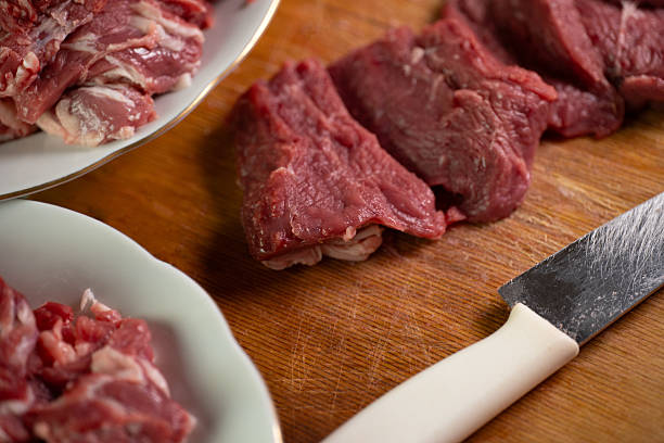 Assorted cuts of raw beef are neatly arranged on a wooden cutting board. A sharp knife lies nearby, highlighting the preparation for a meal in a home kitchen.