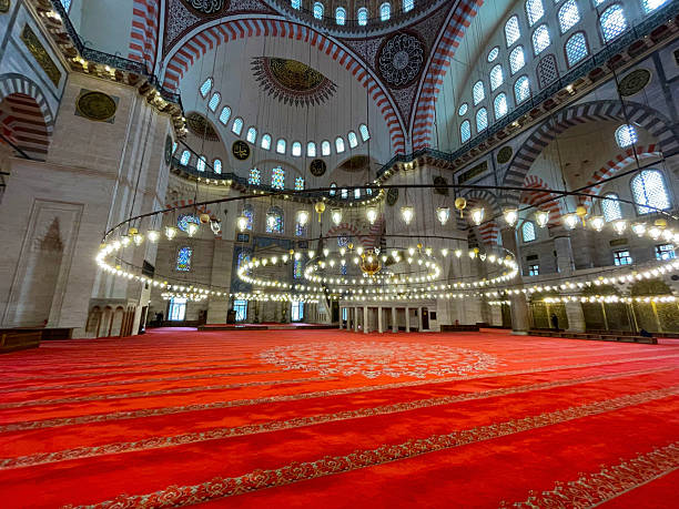 istock Interior of mosque with red carpet rows, golden chandeliers, and domed patterned ceiling 2207538137