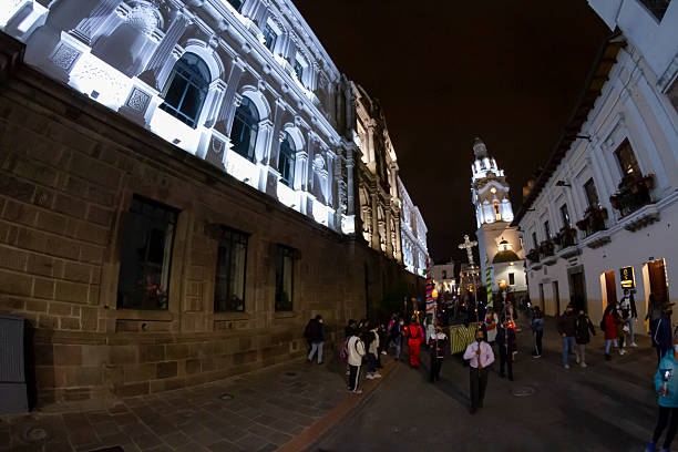 Quito, Pichincha, Ecuador - April 14, 2022: Group of indigenous people walking in a procession during Holy Week celebrations in Quito, Ecuador, with illuminated colonial buildings and a church in the background at night