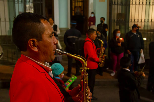 Quito, Pichincha, Ecuador - April 14, 2022: Musician in a red jacket plays the saxophone during a Holy Week procession in Quito, Ecuador, surrounded by other musicians and people holding candles