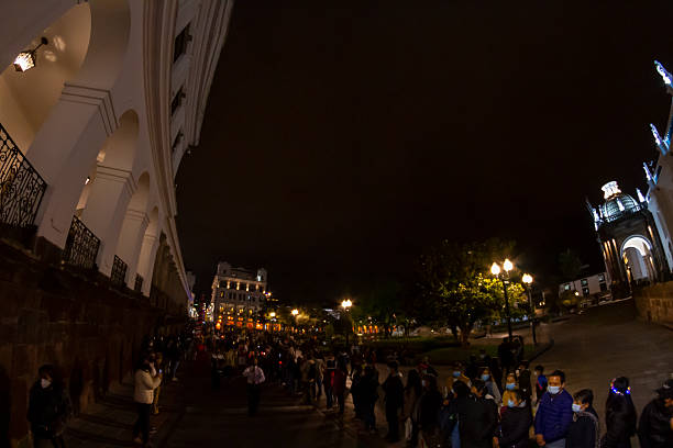 Quito, Pichincha, Ecuador - April 14, 2022: Crowd of people walking in procession during Holy Week celebrations in Quito, Ecuador, wearing face masks and traditional clothing, embodying faith and community spirit under evening lights