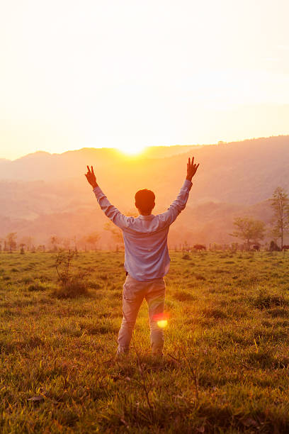 istock Man with raised arms looking at sunset-lit hills 2207548331