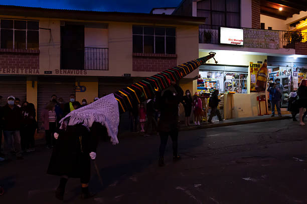 Alangasi, Quito, Pichincha, Ecuador - April 15, 2022: Indigenous people carrying a tall, decorated structure during the traditional Diablos de Alangasi procession, a Holy Week celebration in Quito, Ecuador, with spectators watching from the sidewalks