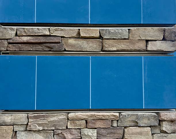textured stone and glossy blue tile cover the exterior building wall in a geometric pattern reflecting sunlight with bold contrast between natural earth tones and vibrant ceramic surfaces