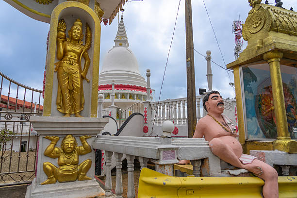 Exterior Buddhist temple decorations including gold and fat man statues with stupa behind from road in Sri Lanka.