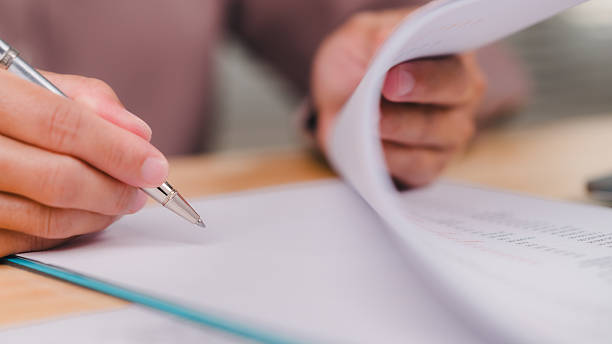 istock Engaging in Document Review, Focused individual reviews important documents, process of careful examination and note-taking with pen in hand 2207577577