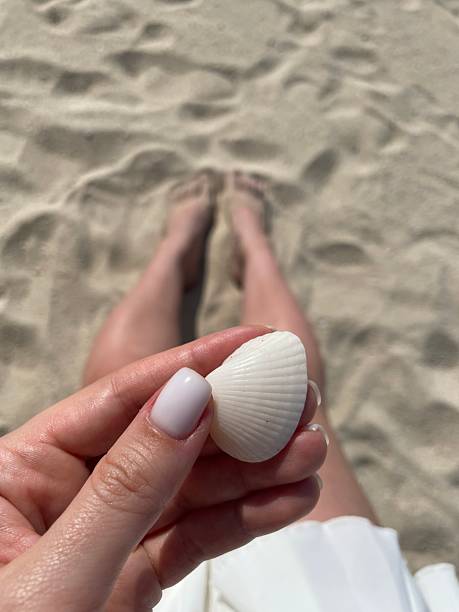 Woman holding a perfect white seashell on a sunny beach, enjoying summer vacation