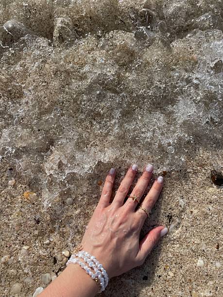 istock Woman's hand touching wet sand on the beach 2207589944