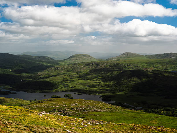 istock The image shows several hills and mountains. A lake is in the foreground. The sky is lightly cloudy with blue patches. 2207599192