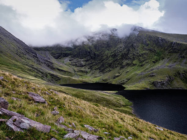 istock Coomloughra Lough is nestled between breathtaking mountains in County Kerry, with clouds drifting overhead. The lush green landscape is a stunning contrast to the dark waters. 2207599217