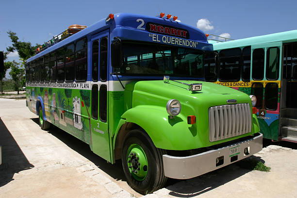 A repurposed and brightly painted old school bus is parked on a dirt road under a blue sky. Used for tourist or local transportation, this bus creates a cheerful and vibrant scene typical of rural Yucatan, Mexico.