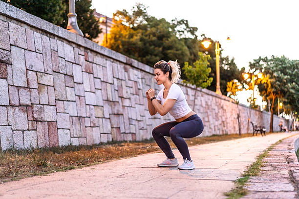 Young sporty woman doing squats outdoors during sunset
