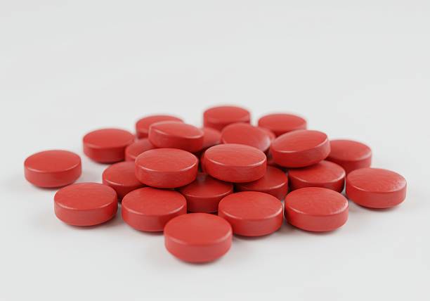 Close-up and selective focus on red pills in amber bottle placed on white wooden table, high angle view