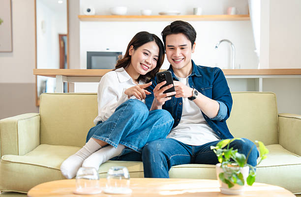 istock Smiling couple enjoying content on a smartphone while relaxing on the couch at home 2207607509